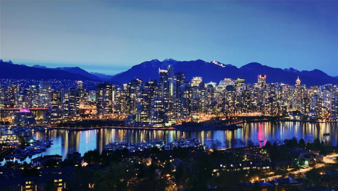 A night time view of beautiful Vancouver. The skyline is illuminated by its skyscapers countless lights infront of dark blue night sky and purple mountains. 